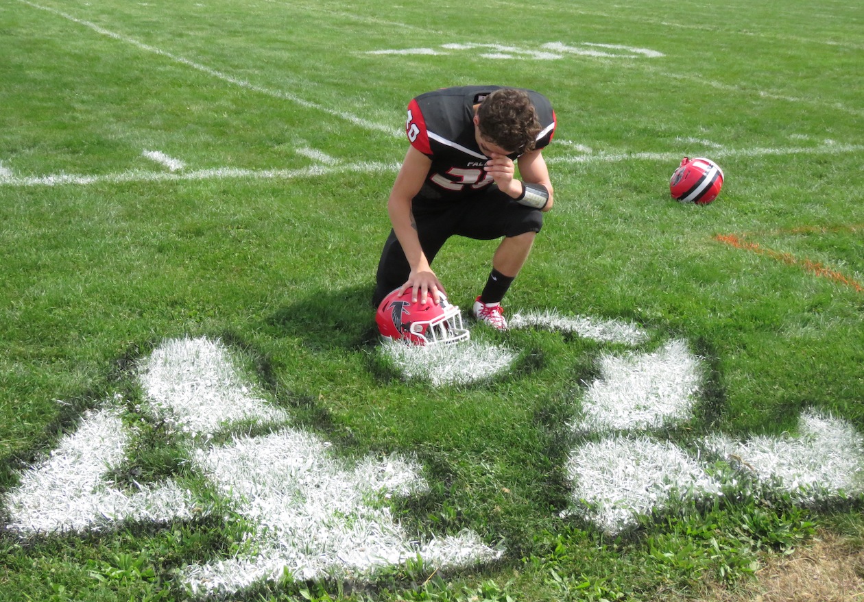 Niagara-Wheatfield's Jake DeWolf takes a knee by a paint No. 42 to remember the life of Michael Ziegler before the Falcons' opening football game versus North Tonawanda. N-W defeated the Lumberjacks, 48-0. (Photo by David Yarger)